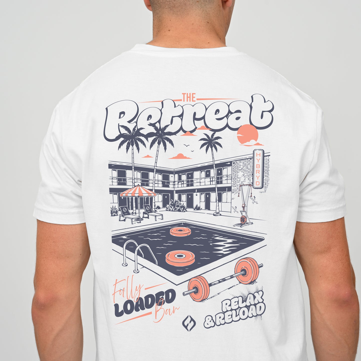 A crossFit athlete wearing a white t-shirt, viewed from the back. The shirt features a large graphic print of a retro motel pool scene with palm trees, a bar, and gym equipment, with text reading 'The Retreat', 'Fully Loaded Bar', and 'Relax & Reload'.
