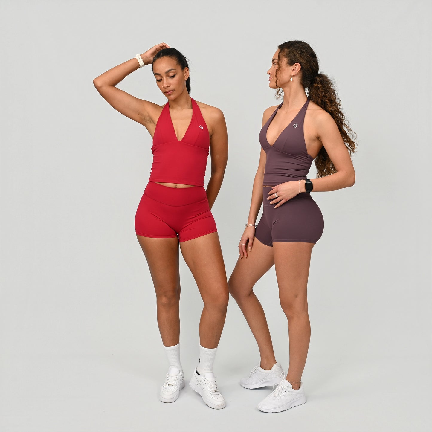 Two women wearing red and purple athletic crossfit outfits on a plain background