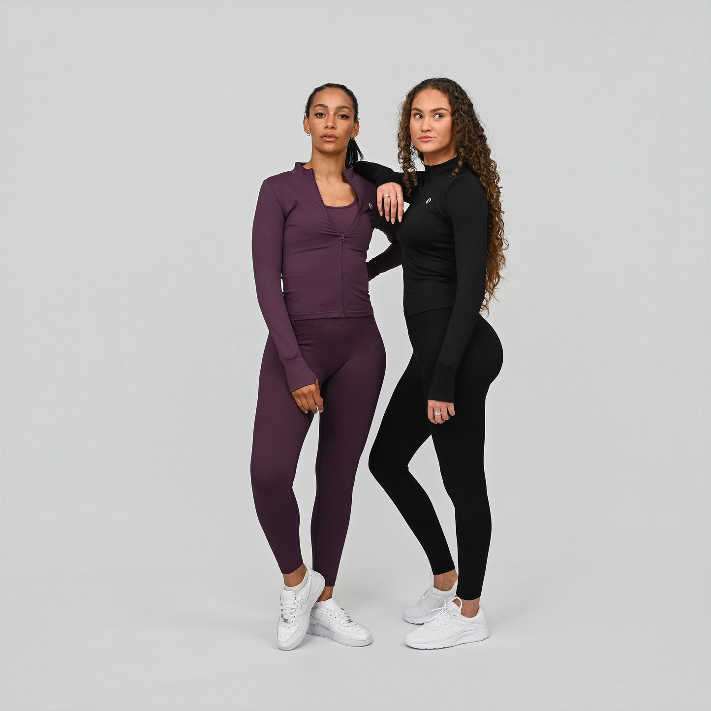 Two women wearing matching athletic crossfit outfits with compression waist leggings on a plain background