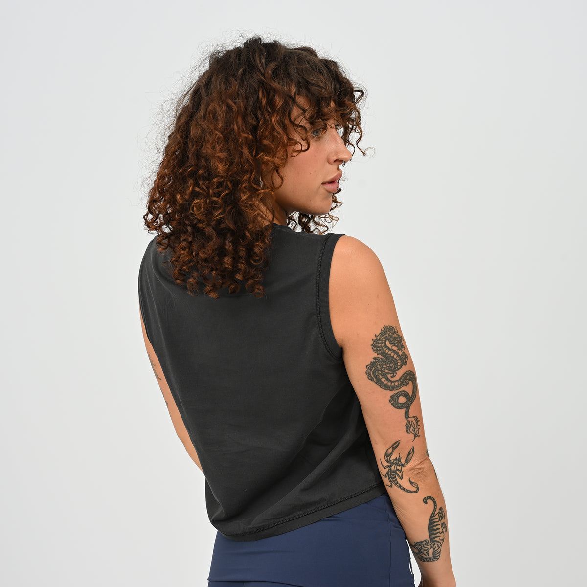 A woman wearing a HYBRYD Zara women’s black cropped gym tank vest in enzyme-washed organic cotton, relaxed fit sleeveless training top for HYROX and functional fitness.