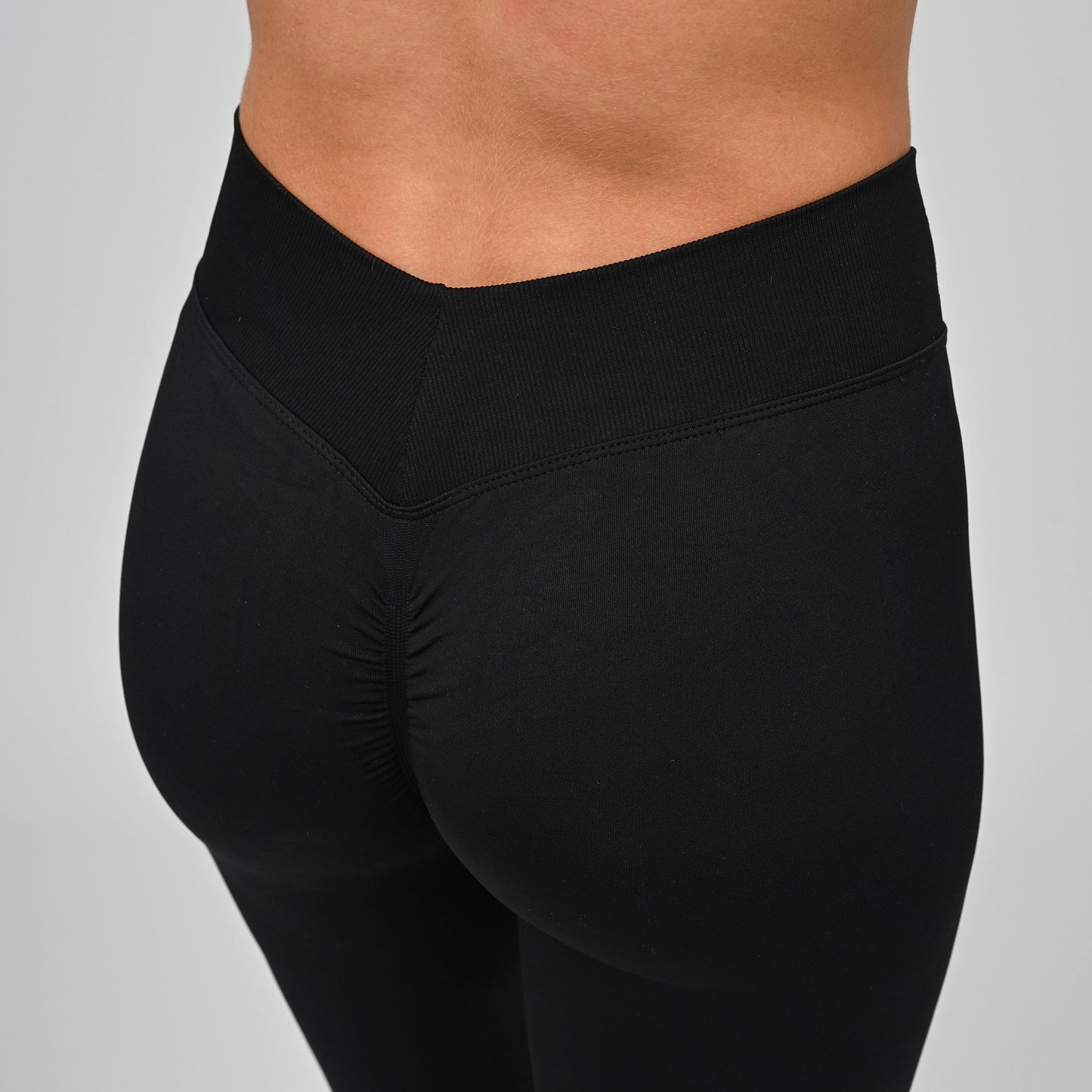 Close up shot of a girls bum wearing black Hybryd equinox leggings that have a v-dip rear waist and a scrunch bum. From activewear brand Hybryd