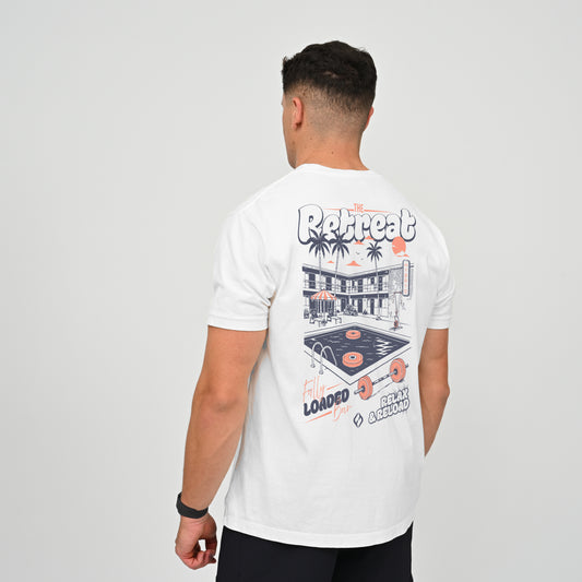 A crossfit athlete wearing a white graphic t-shirt, viewed from behind to show the back print. The graphic features a retro diner, palm trees, a vinyl record, and text reading Hybryd Retreat.