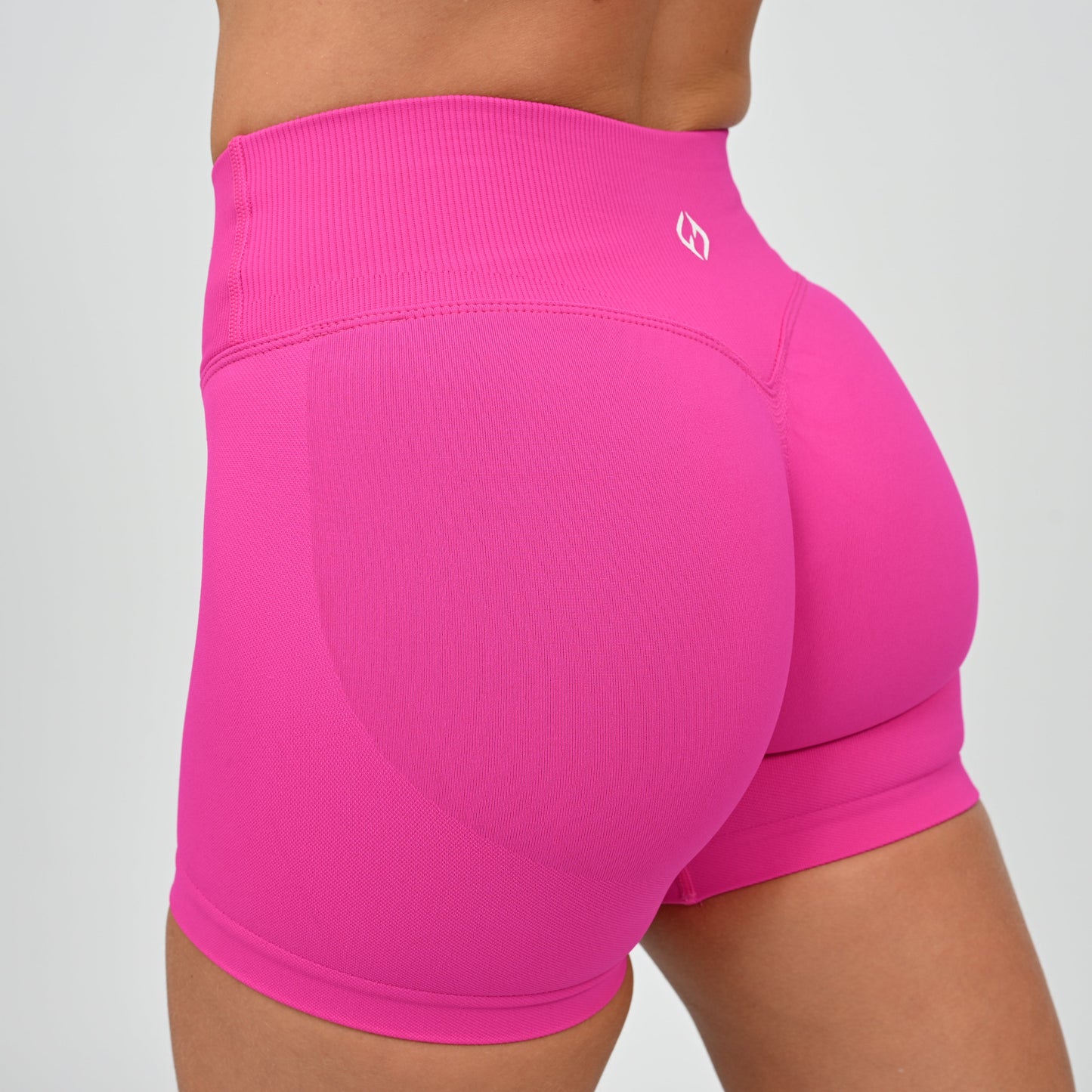 Crossfit athlete wearing a candy pink pair of booty shorts. Crossover waist and cinch bum. Contour shading  around the bum. Made by gymwear and activewear brand Hybryd