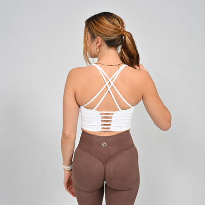A Hyrox athlete wearing a white long line sports bra with brown leggings.  Pictured from the rear showing off the strappy back. Made by the gymwear brand Hybryd.