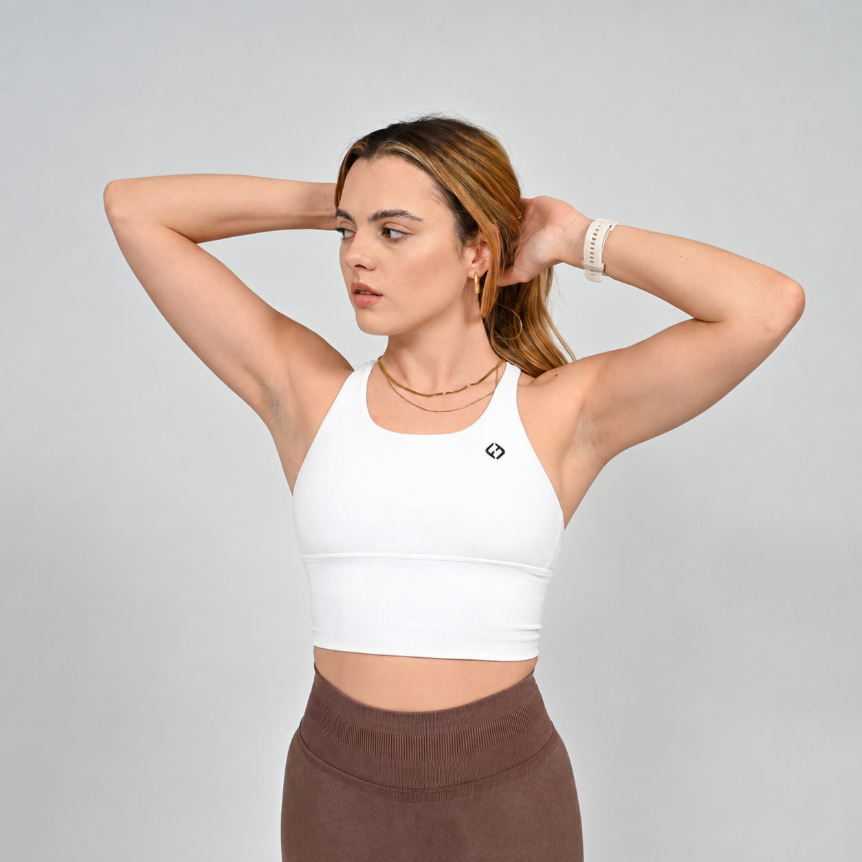 A Hyrox athlete wearing a white long line sports bra with brown leggings. Made by the gymwear brand Hybryd.