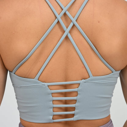Close-up back view of a person wearing a light blue-gray strappy sports bra  from Hybryd with crisscross straps and cutout details at the lower back.