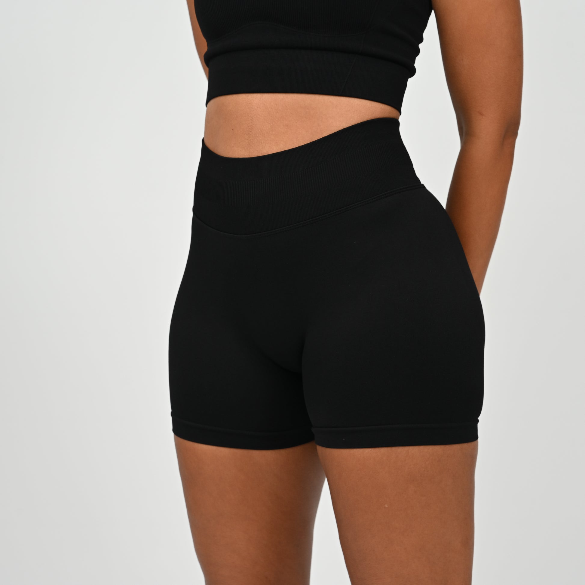 Hyrox woman wearing black, high waisted, cinch bum workout bootie shorts with contouring. Teamed with a matching muscle back sports bra. From activewear brand Hybryd