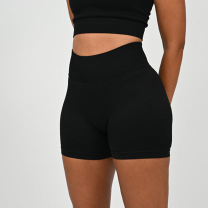 Hyrox woman wearing black, high waisted, cinch bum workout bootie shorts with contouring. Teamed with a matching muscle back sports bra. From activewear brand Hybryd