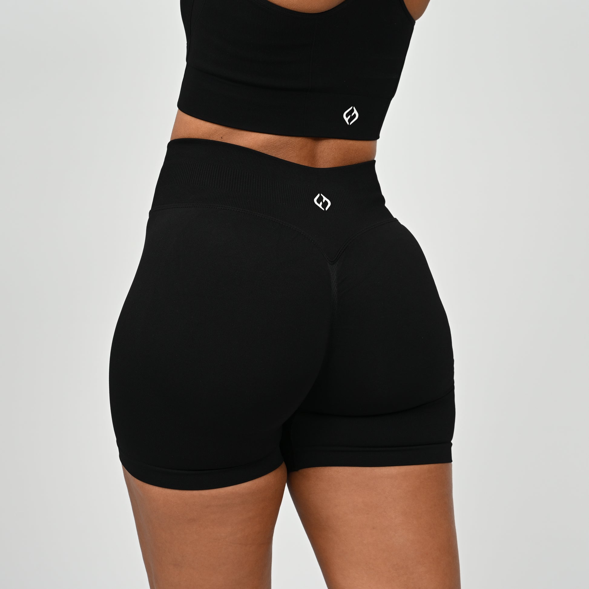 Hyrox woman wearing black, high waisted, cinch bum workout bootie shorts with contouring. Teamed with a matching muscle back sports bra. From activewear brand Hybryd