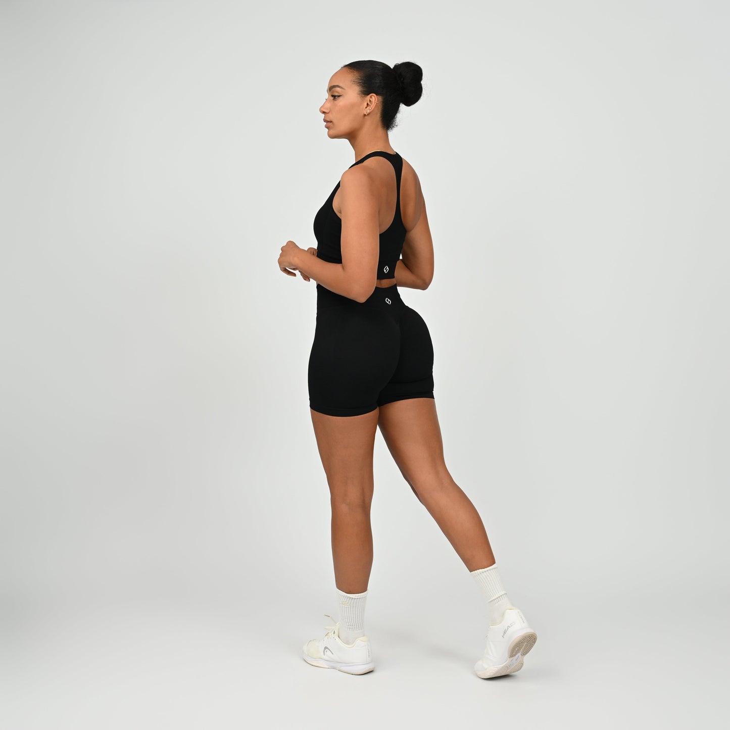 Hyrox woman wearing black, high waisted, cinch bum workout bootie shorts with contouring. Teamed with a matching muscle back sports bra. From activewear brand Hybryd