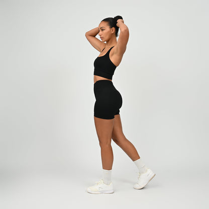 Hyrox woman wearing black, high waisted, cinch bum workout bootie shorts with contouring. Teamed with a matching muscle back sports bra. From activewear brand Hybryd