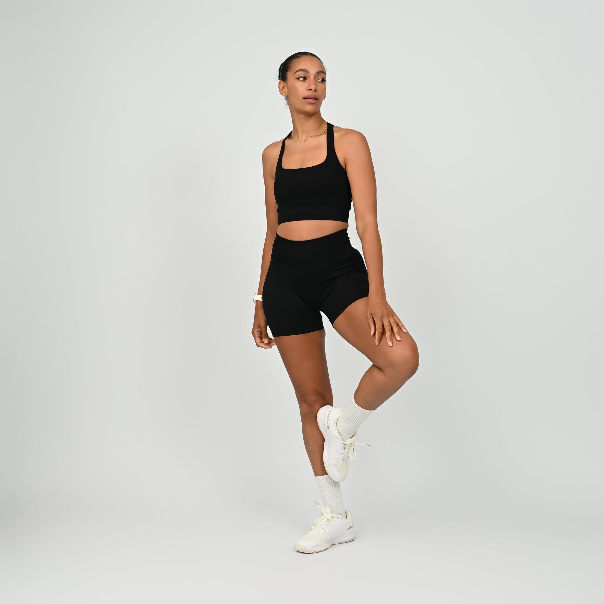 Hyrox woman wearing black, high waisted, cinch bum workout bootie shorts with contouring. Teamed with a matching muscle back sports bra. From activewear brand Hybryd