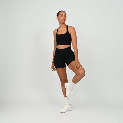 Hyrox woman wearing black, high waisted, cinch bum workout bootie shorts with contouring. Teamed with a matching muscle back sports bra. From activewear brand Hybryd