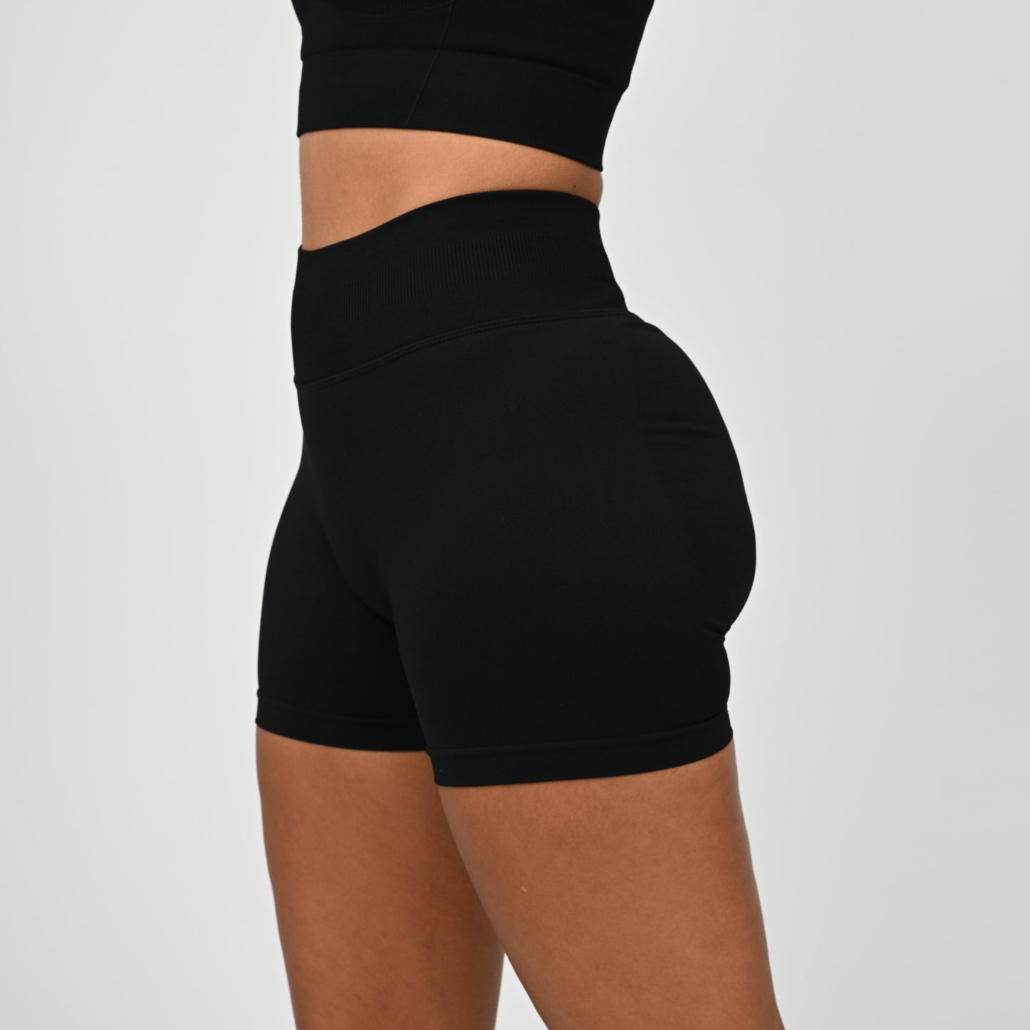 Hyrox woman wearing black, high waisted, cinch bum workout bootie shorts with contouring. Teamed with a matching muscle back sports bra. From activewear brand Hybryd