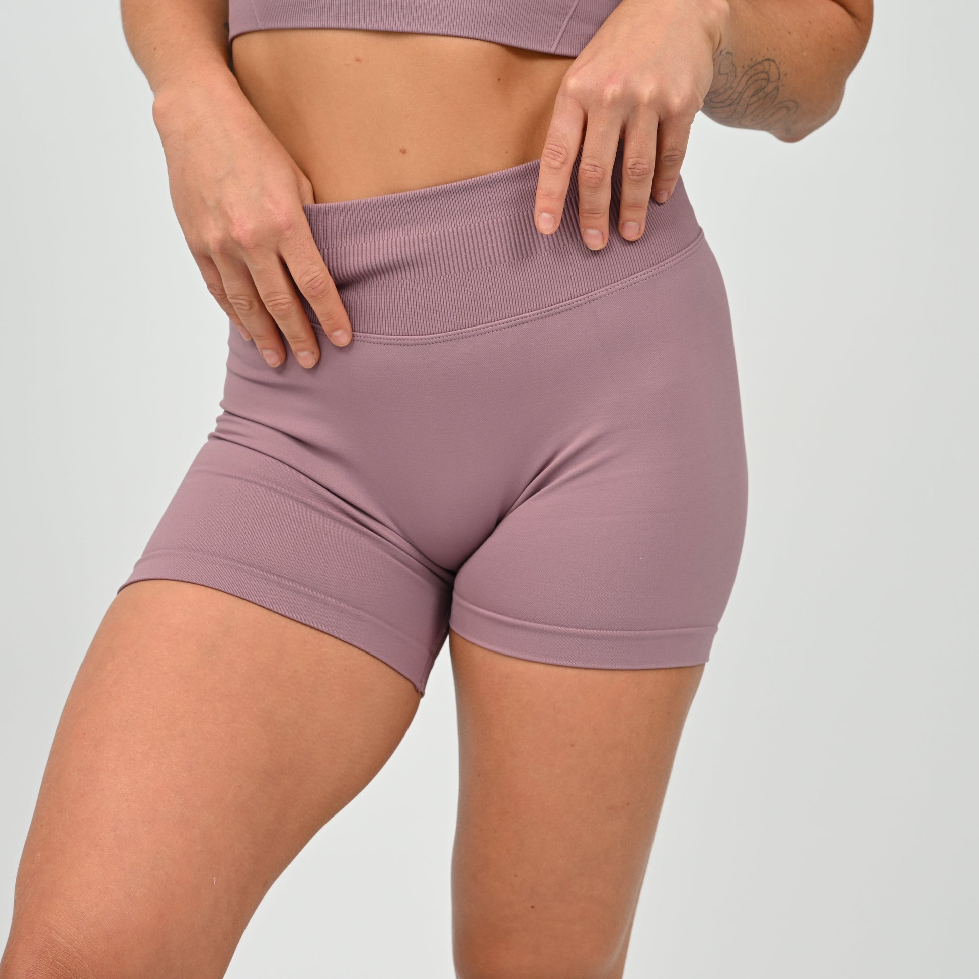 Hyrox woman wearing mauve, high waisted, cinch bum workout bootie shorts with contouring. Teamed with a matching muscle back sports bra. From activewear brand Hybryd