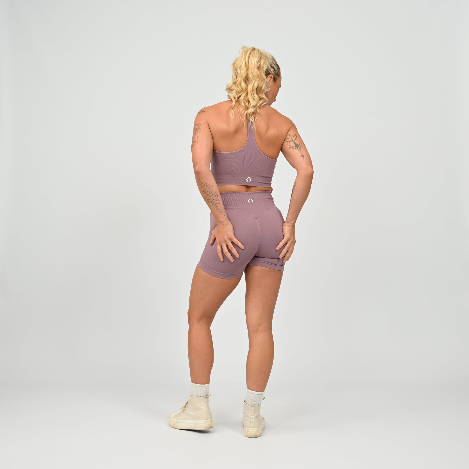 Hyrox woman wearing a mauve, high waisted, cinch bum workout bootie shorts with contouring. Teamed with a matching muscle back sports bra. From activewear brand Hybryd