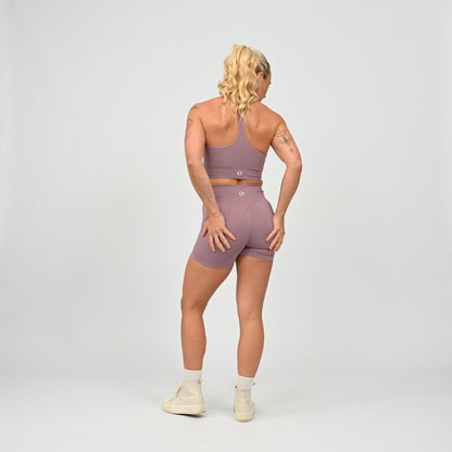 Hyrox woman wearing a mauve, high waisted, cinch bum workout bootie shorts with contouring. Teamed with a matching muscle back sports bra. From activewear brand Hybryd