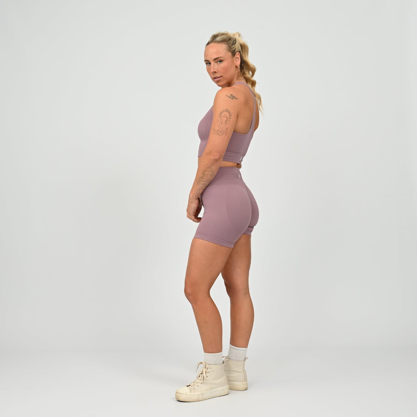 Hyrox woman wearing a mauve, high waisted, cinch bum workout bootie shorts with contouring. Teamed with a matching muscle back sports bra. From activewear brand Hybryd