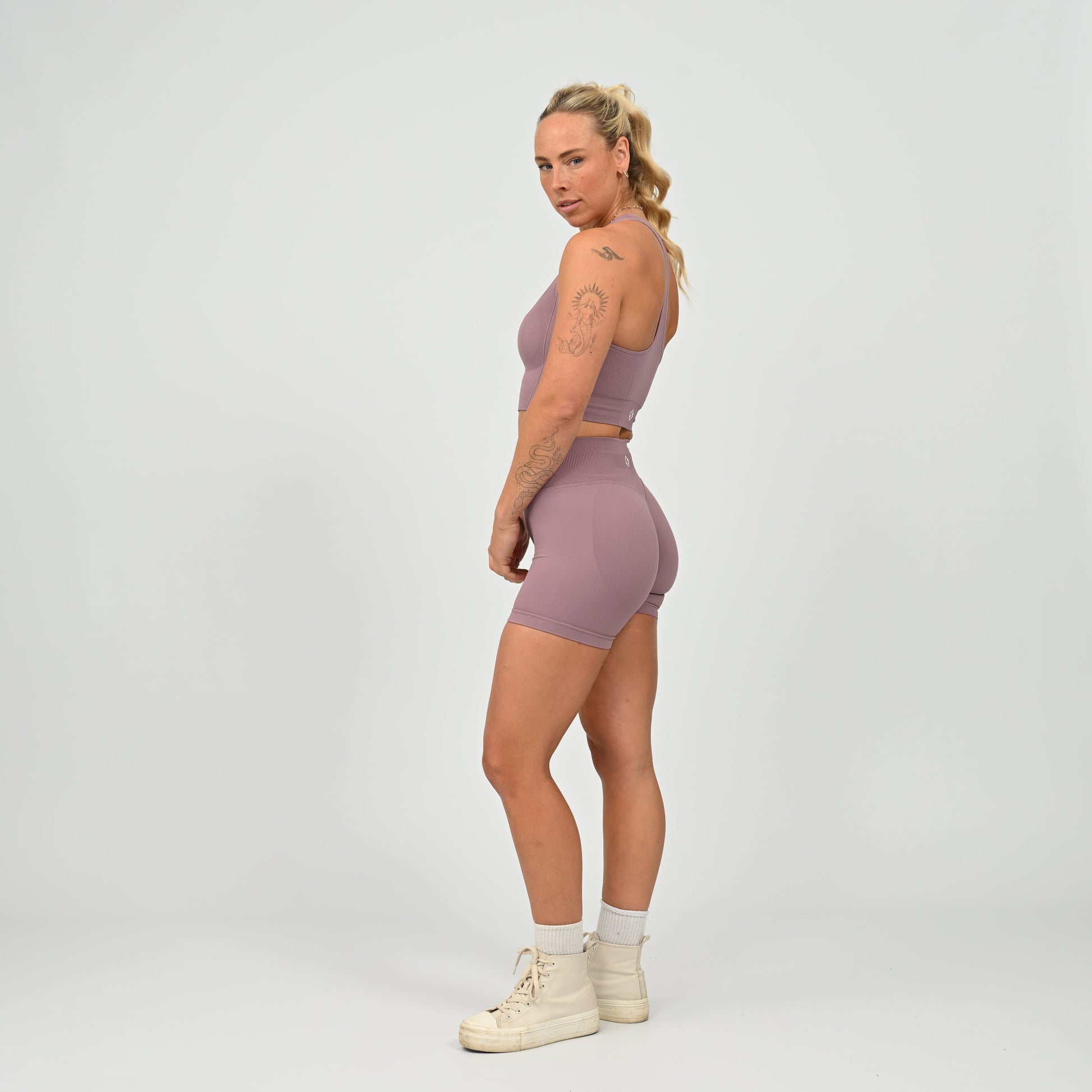 Hyrox woman wearing a mauve, high waisted, cinch bum workout bootie shorts with contouring. Teamed with a matching muscle back sports bra. From activewear brand Hybryd