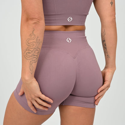 Hyrox woman wearing a mauve, high waisted, cinch bum workout bootie shorts with contouring. Teamed with a matching muscle back sports bra. From activewear brand Hybryd