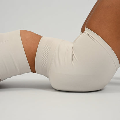 Hyrox woman wearing off white, high waisted, cinch bum workout bootie shorts with contouring. Teamed with a matching muscle back sports bra. From activewear brand Hybryd