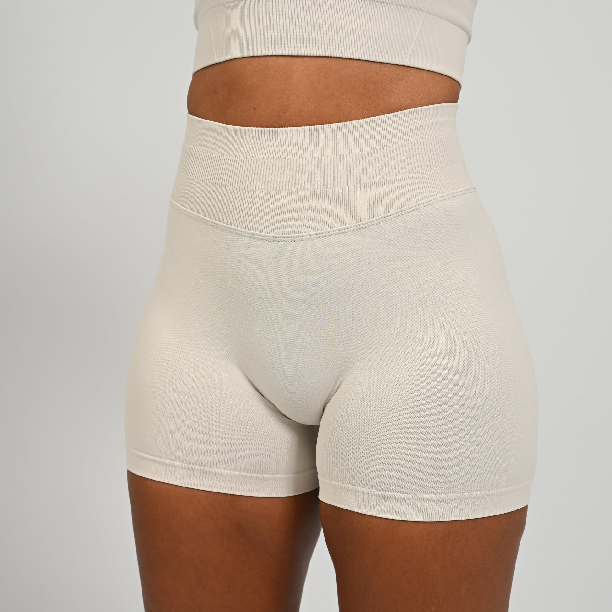 Hyrox woman wearing off white, high waisted, cinch bum workout bootie shorts with contouring. From activewear brand Hybryd
