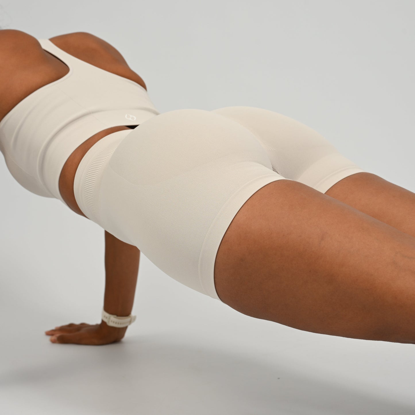 Hyrox woman wearing off white, high waisted, cinch bum workout bootie shorts with contouring. Teamed with a matching muscle back sports bra. In a press up posistion. From activewear brand Hybryd