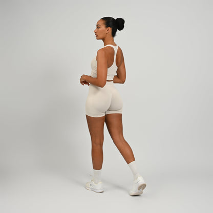 Hyrox woman wearing off white, high waisted, cinch bum workout bootie shorts with contouring. Teamed with a matching muscle back sports bra. From activewear brand Hybryd