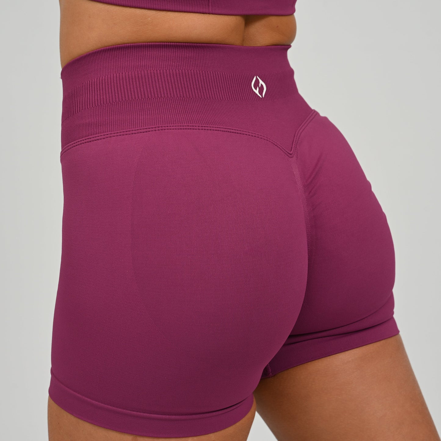 Hyrox woman wearing purple, high waisted, cinch bum workout bootie shorts with contouring. Teamed with a matching muscle back sports bra. From activewear brand Hybryd