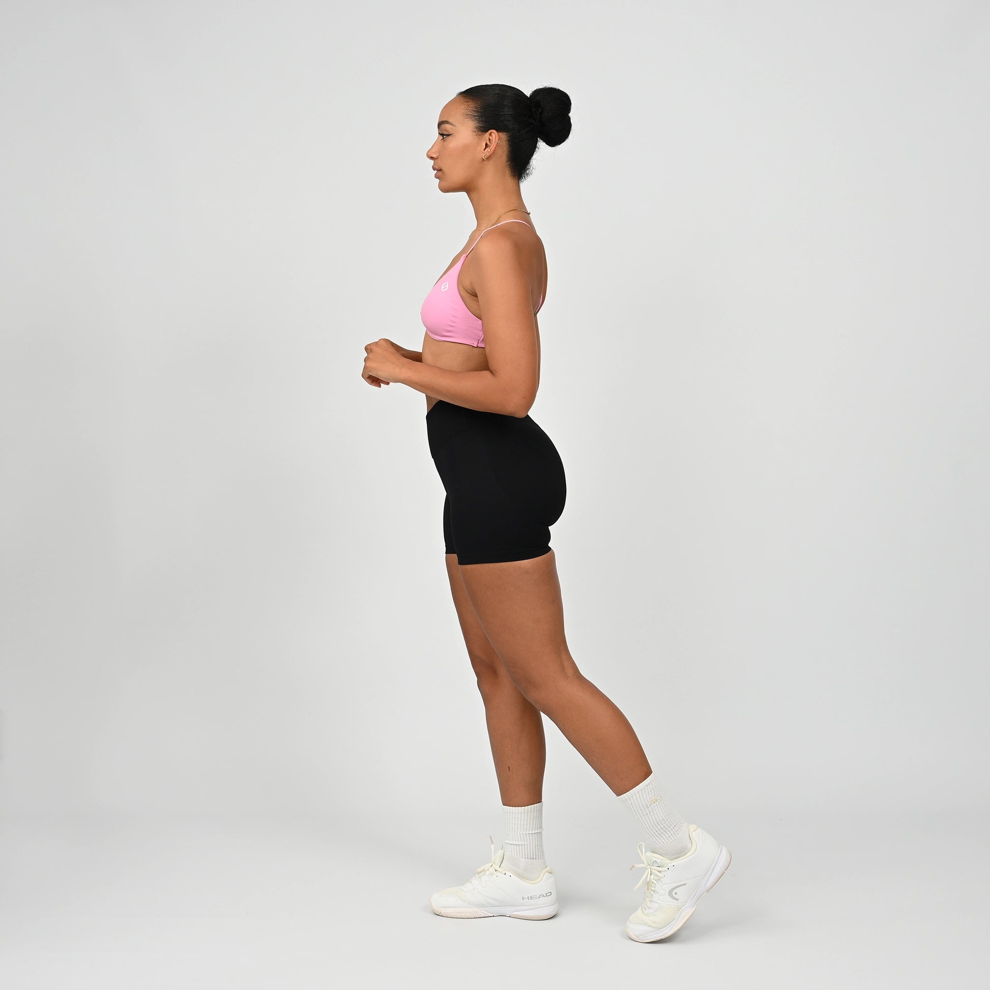 Gym girl wearing a pink minimal sports bra with crossover front. Worn with scrunch bum bootie shorts that have a crossoer waistband.  Made by the activewear brand Hybryd.