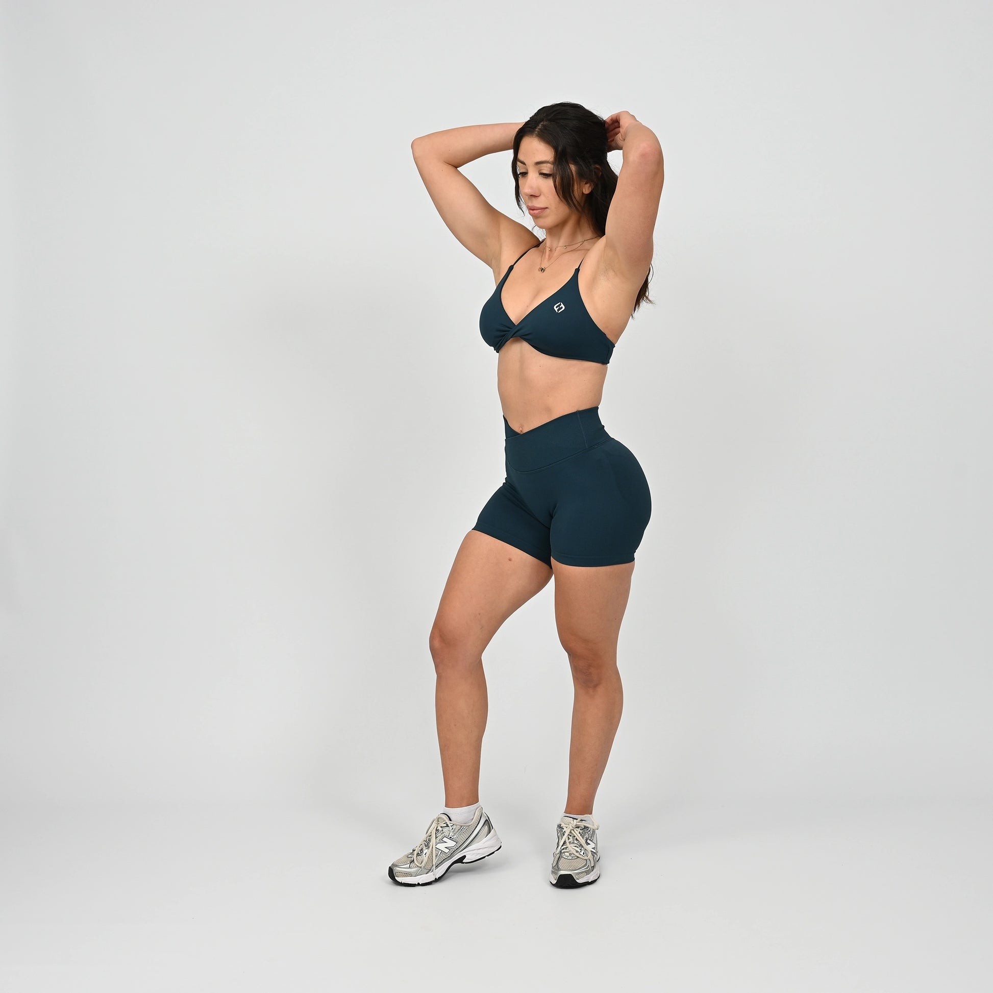 Gym girl wearing a dark green minimal sports bra with crossover front. Worn with scrunch bum bootie shorts.  Made by the activewear brand Hybryd.