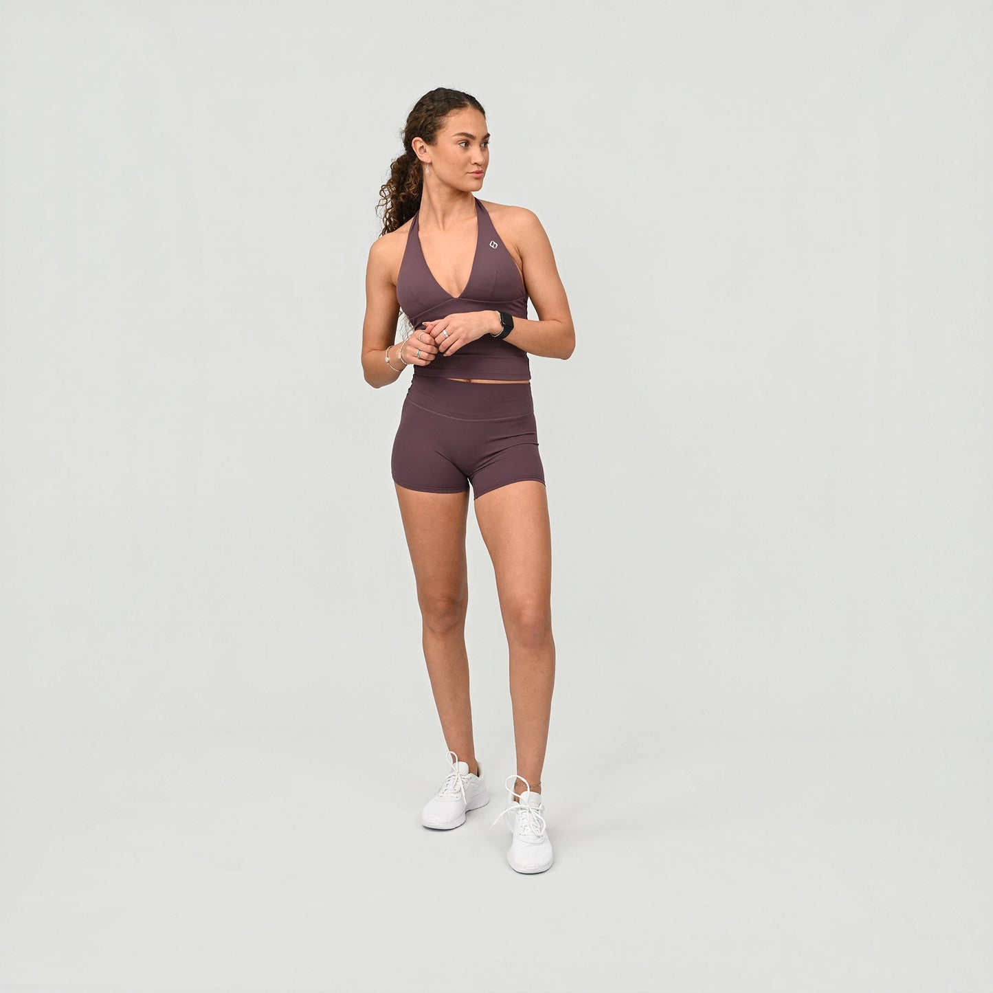 Woman wearing a purple athletic gym booty shorts and bra outfit from Hybryd sports wear on a light grey background