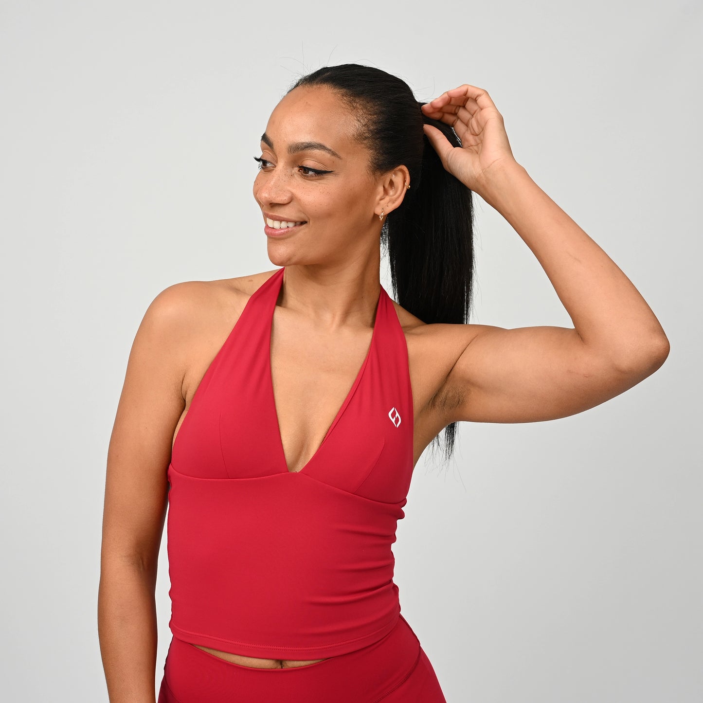 Woman wearing a red sports bra vest and bootys with a Hybryd logo on a grey background