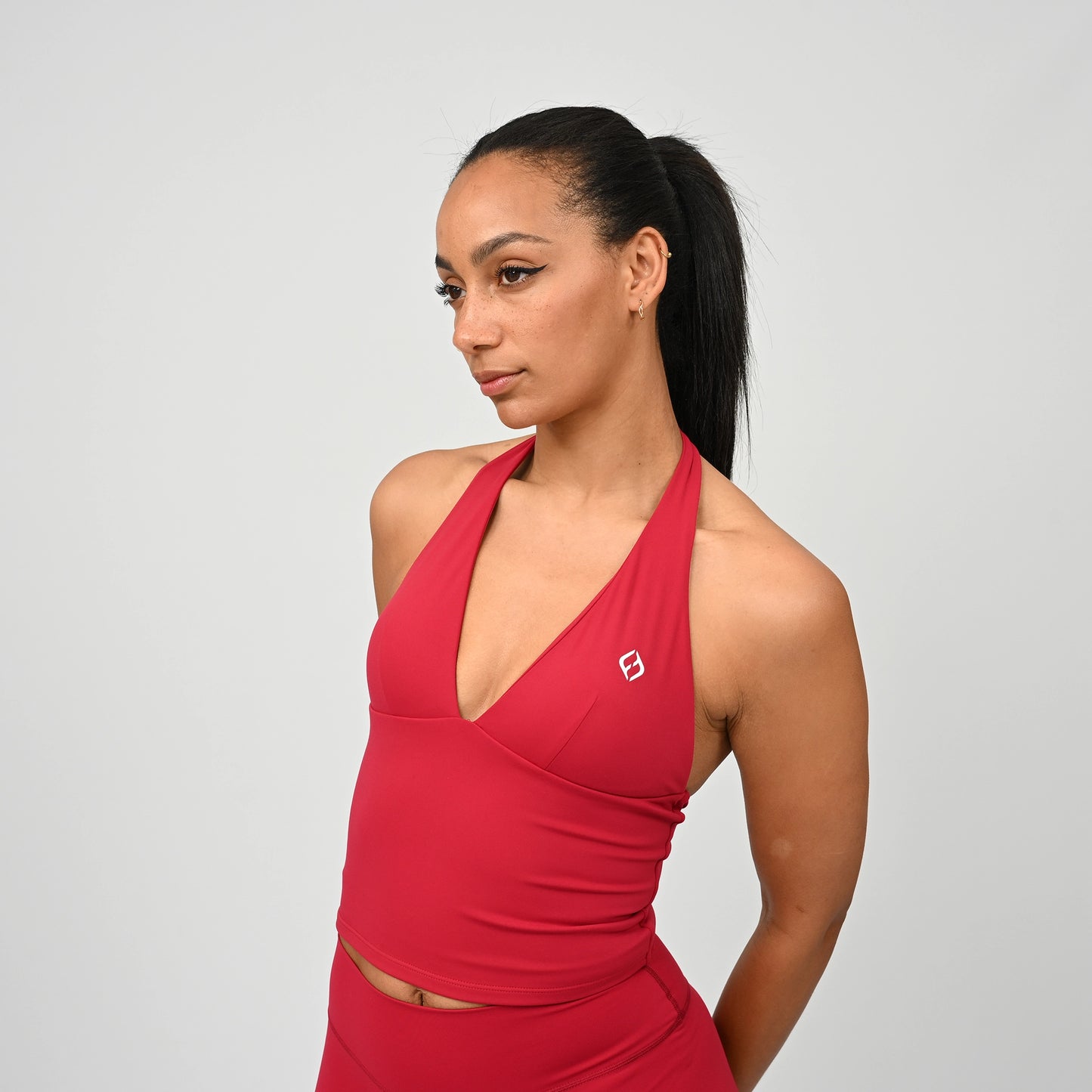 Woman wearing a red sports matching outfit with a padded top and logo on a light grey background. This set is made by Hybryd.