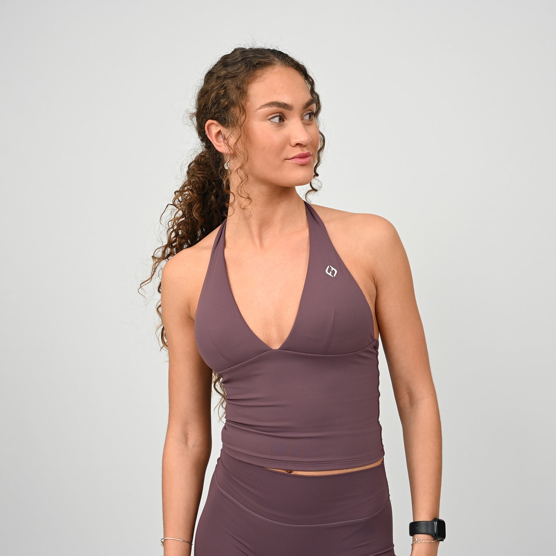 Woman wearing a purple sports bra vest and bootys from Hybryd on a light grey background.