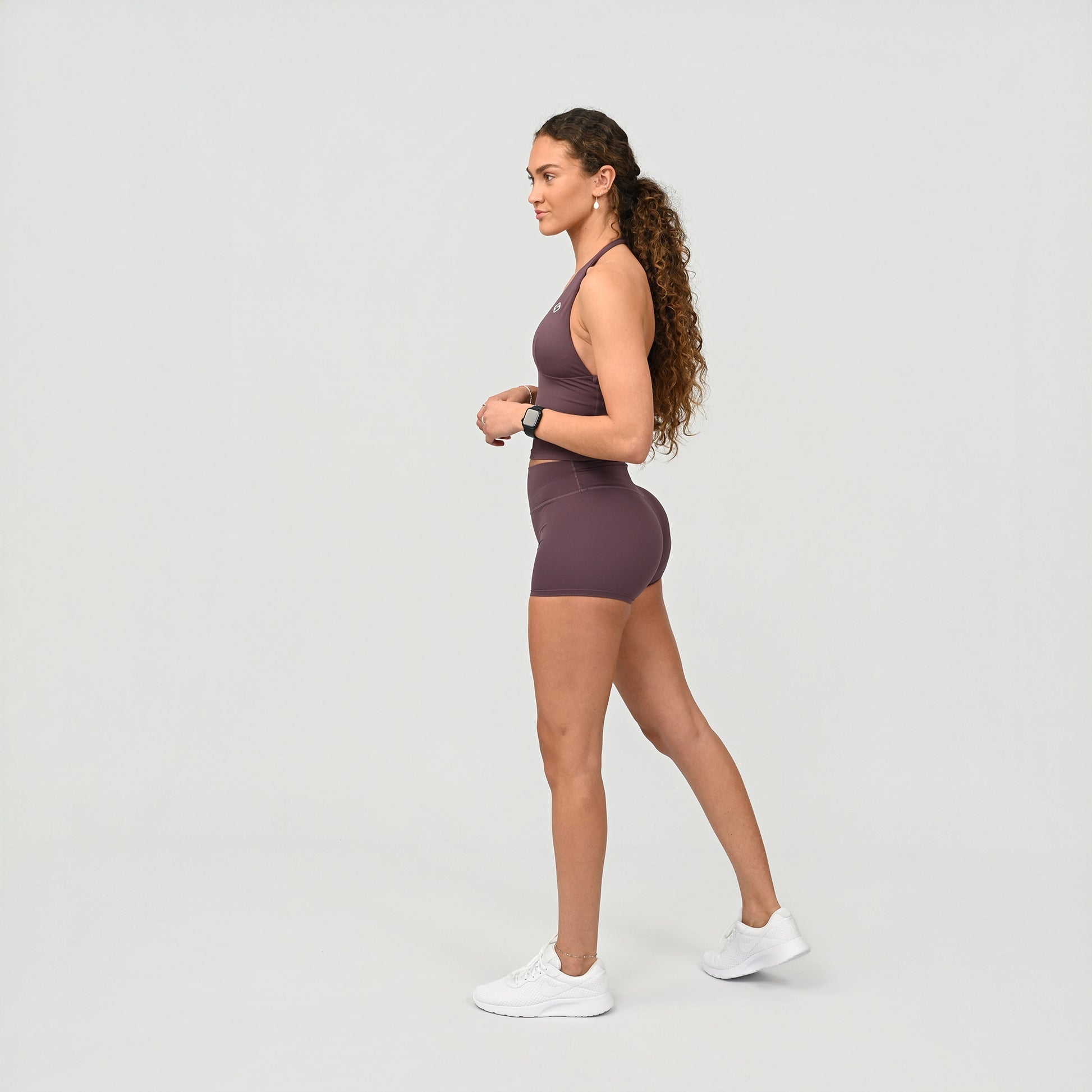 Woman wearing a mauve athletic gym bra and booty shorts on a light gray background from the gymwear brand Hybryd.