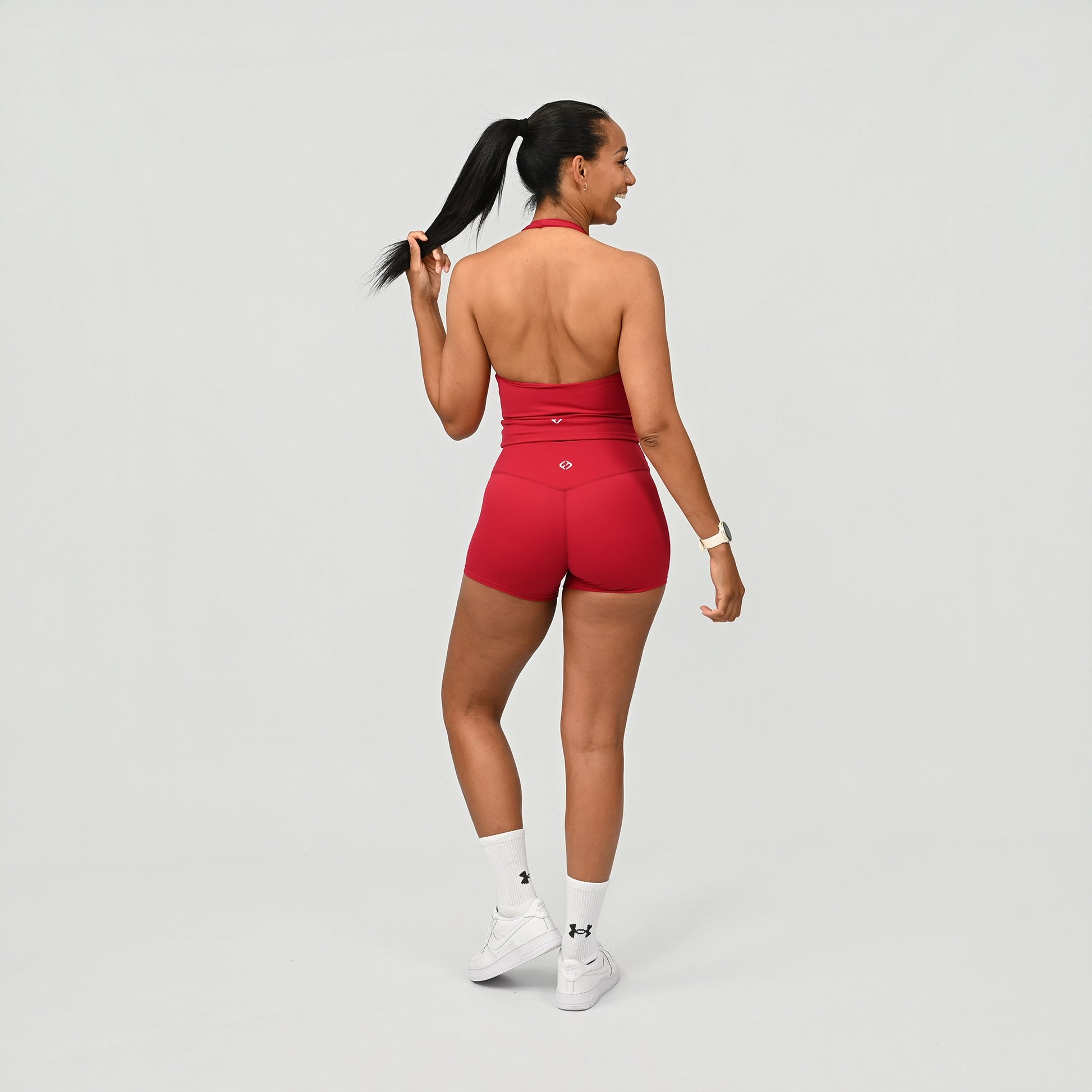 Person wearing a Hybryd red sports outfit with booty shorts and vest on a grey background