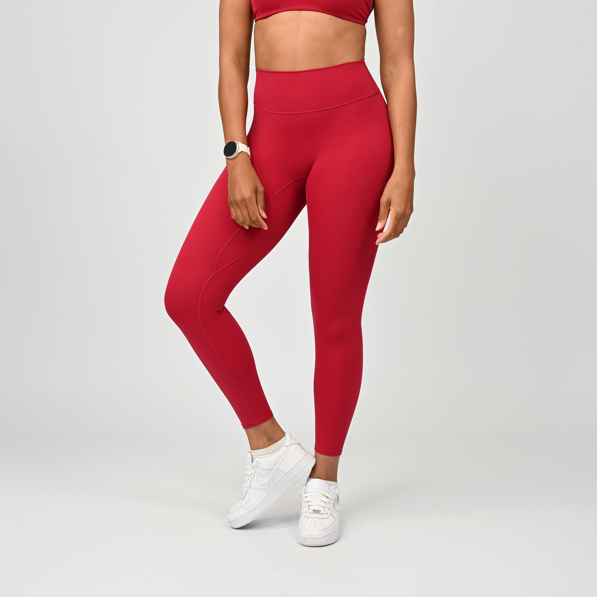 Person wearing Hybryd red gym leggings and white sneakers on a light gray background