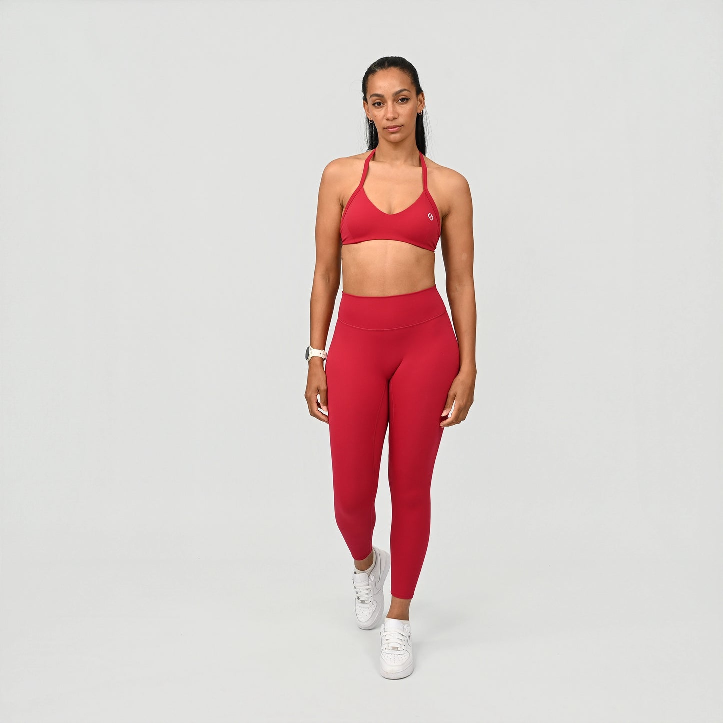 Woman wearing a red halter sports bra and leggings set on a gray background