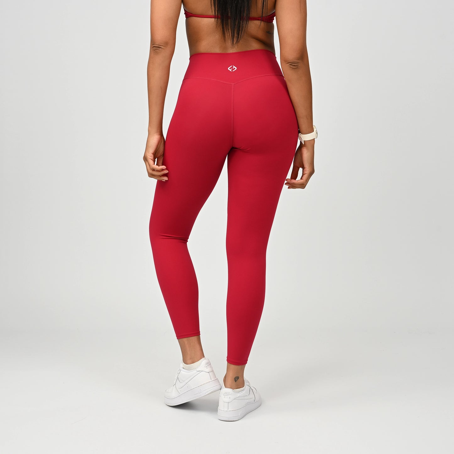 Person wearing red active wear Hybryd leggings and white sneakers on a plain background
