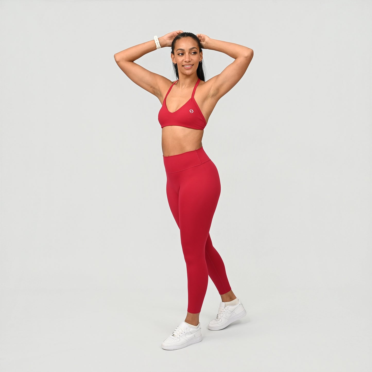 Woman wearing a red gym athletic outfit with Hybryd logo on a light gray background