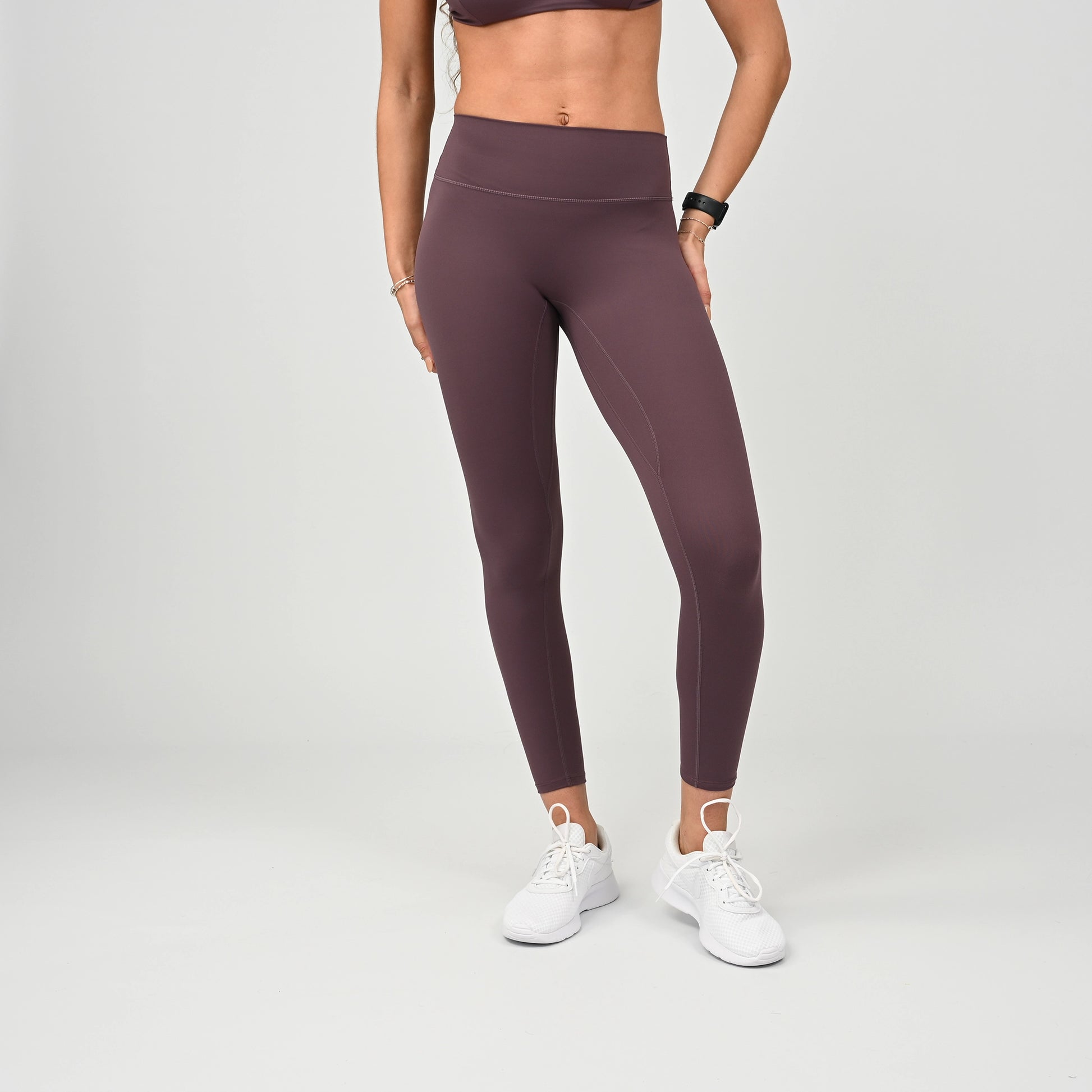 Person wearing maroon workout  leggings and white sneakers on a plain background