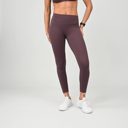 Person wearing maroon workout  leggings and white sneakers on a plain background