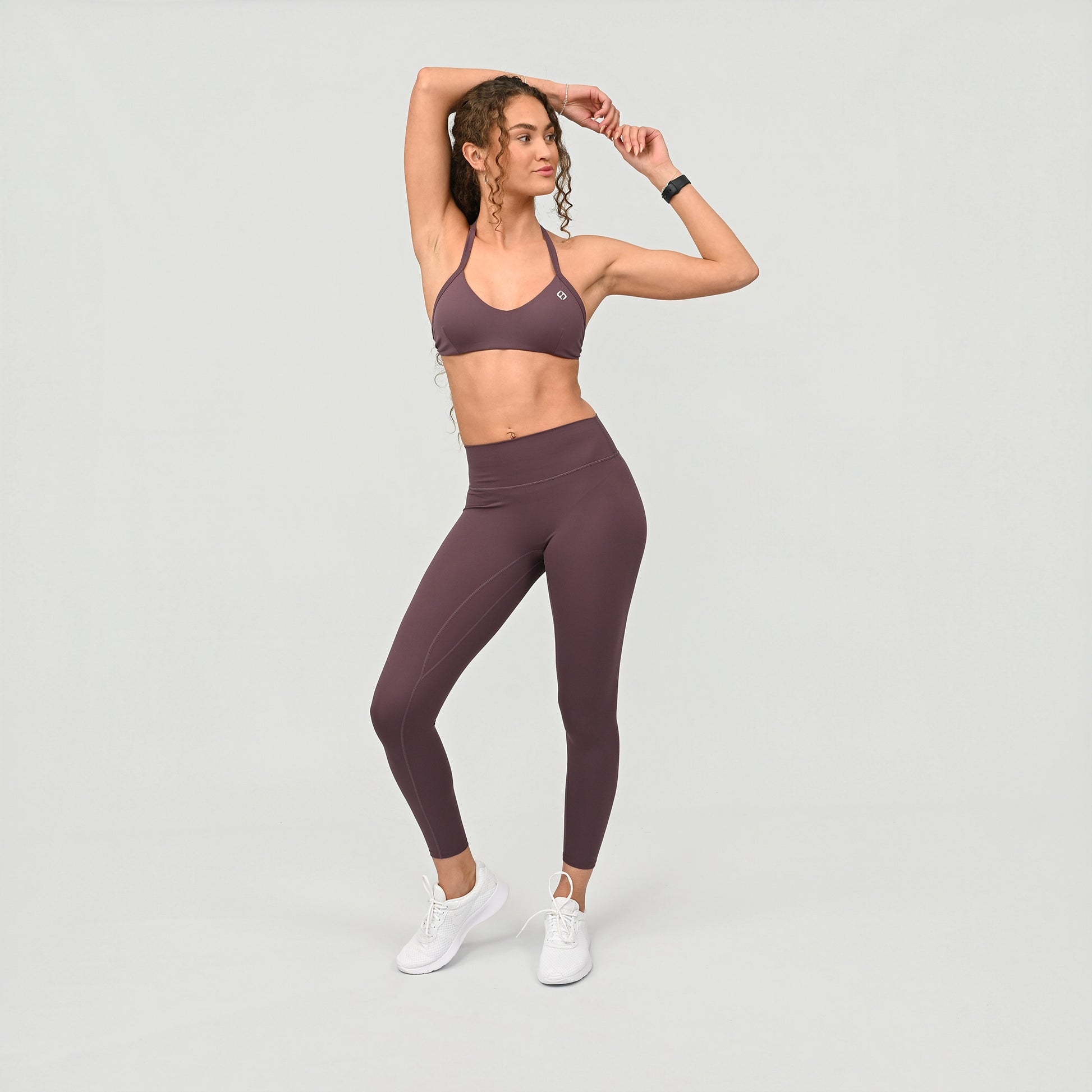 Woman wearing a purple sports halter bra and leggings set on a light gray background from activewear brand Hybryd.