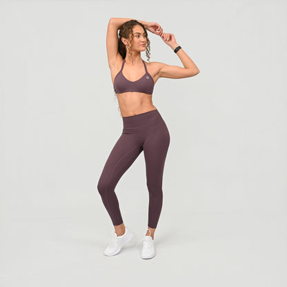 Woman wearing a purple sports halter bra and leggings set on a light gray background from activewear brand Hybryd.