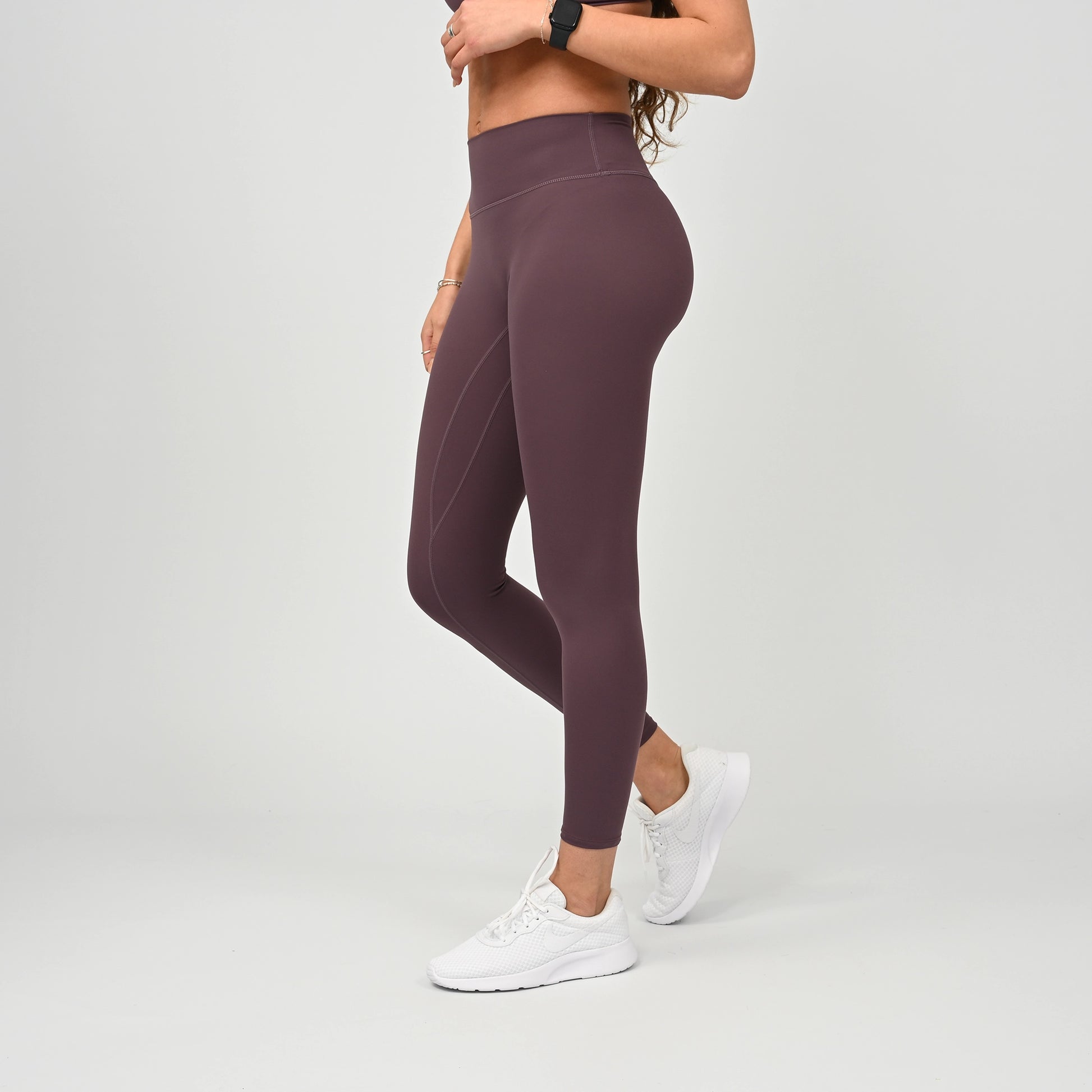 Person wearing soft maroon gym leggings and white sneakers on a light gray background