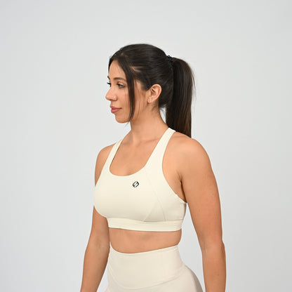 A Hyrox woman in a side profile wearing a cream-colored athletic sports bra and matching high-waisted shorts against a light gray studio background.  From Hybryd.