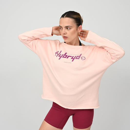 Woman wearing a light pink long-sleeve shirt with 'hybryd' logo on a gray background