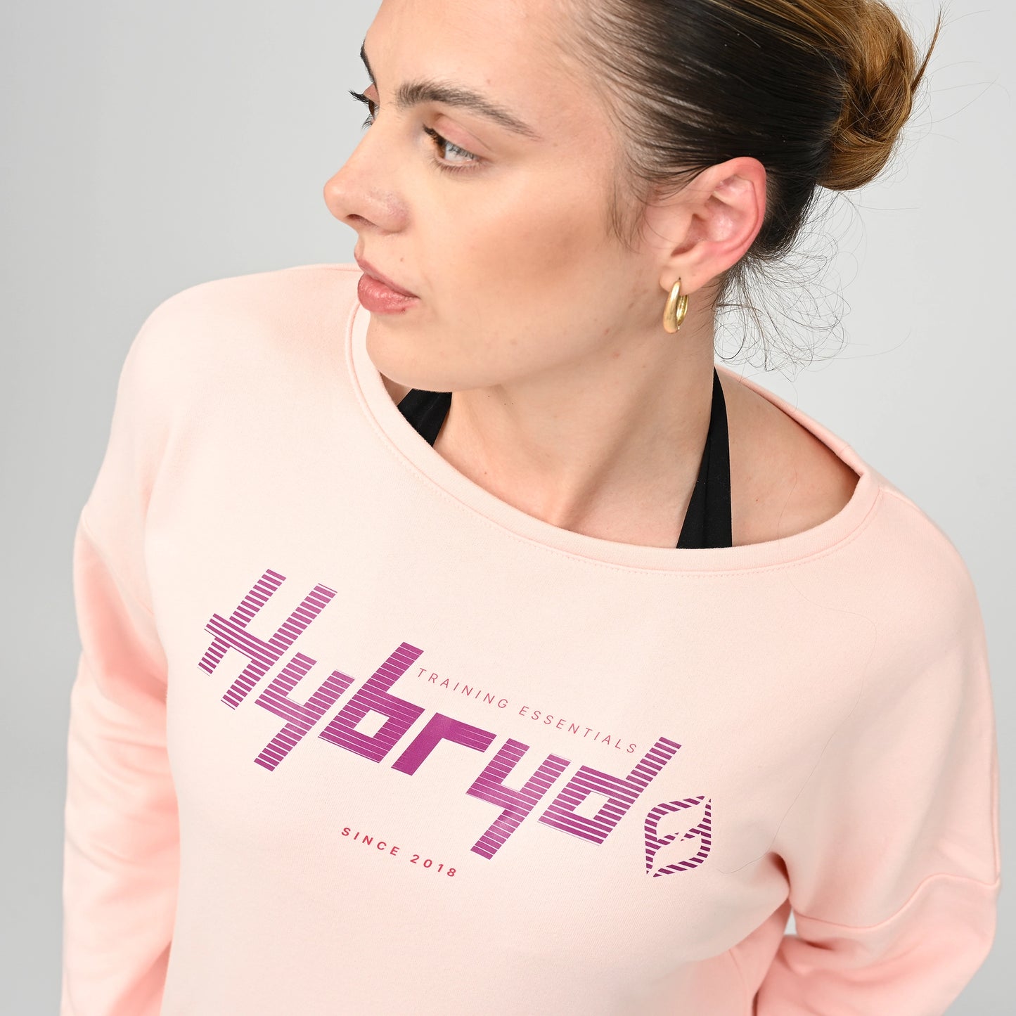 Woman wearing a pink sweatshirt with 'Hybryd' branding on. 