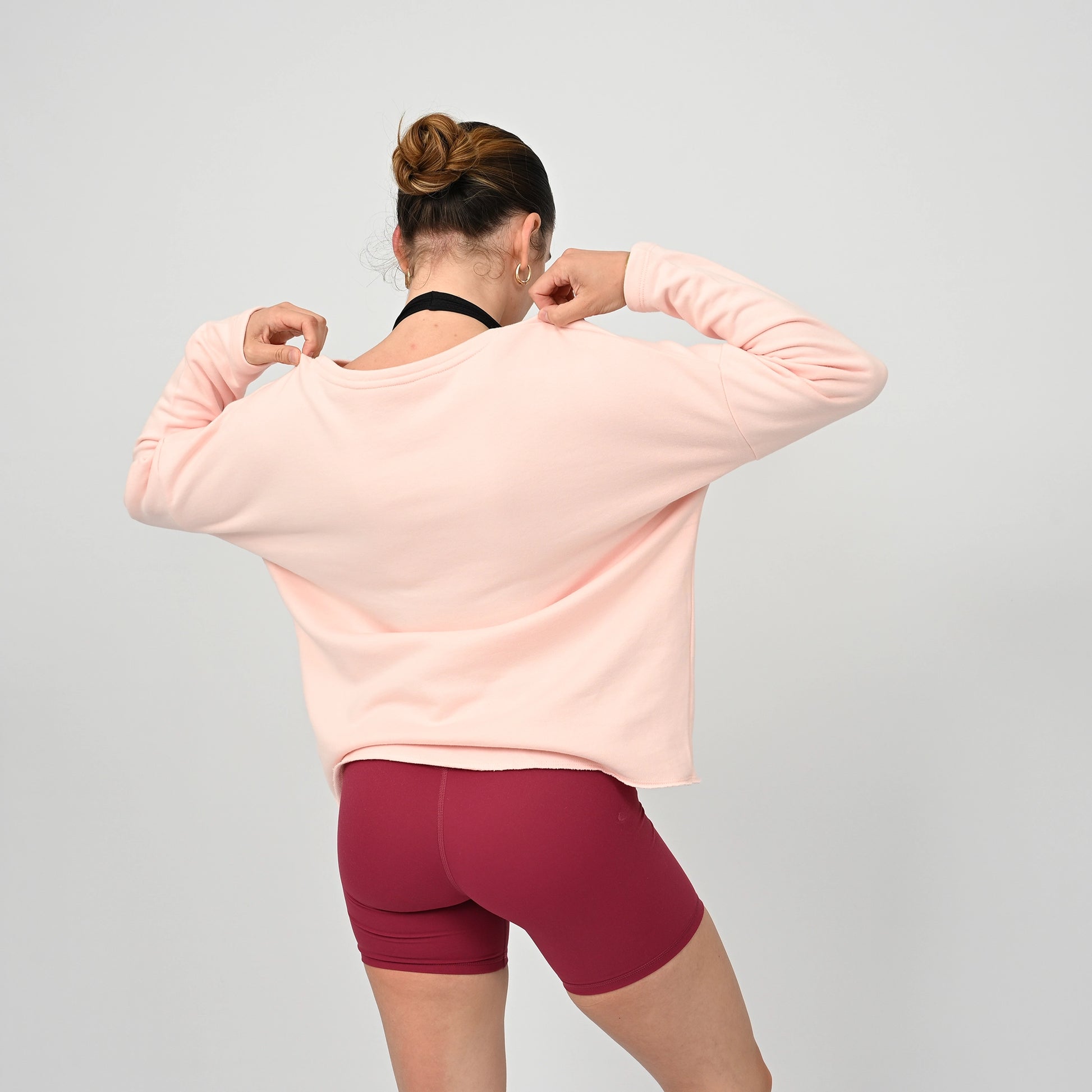 Person wearing a light pink Hybryd sweatshirt and maroon booty shorts on a gray background